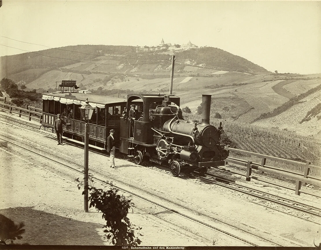 Die Zahnradbahn auf den Kahlenberg, auf dem Talgleis für die Aufnahme der Fotografie unterhalb der Station Grinzing zum Halt gekommen, Fotografie von Michael Frankenstein, 1875, Wien Museum. Das Ziel der Reise wird hier optisch mit dem Beförderungsmittel in unmittelbaren Zusammenhang gesetzt. Die Komposition erinnert an die oben gezeigten Darstellungen der Ritte auf den Kahlenberg, in denen das Ziel des Weges ebenfalls über den Reitenden im Hintergrund zu vernehmen ist (Clarot, „Lustritt auf dem Kahlenberg nächst Wien. Die Caravane im Zuge“ und „Der Ritt nach dem Kahlenberg“, im Verlag Matthäus Trentsensky).