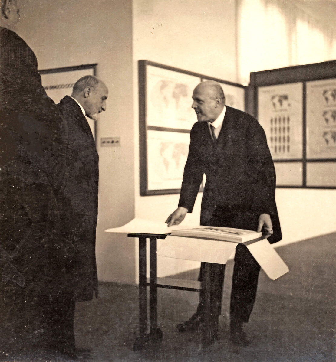 Otto Neurath präsentiert Bürgermeister Karl Seitz das Mappenwerk „Gesellschaft und Wirtschaft“ während der Eröffnung der Ausstellung „Weltwirtschaft“ in den Räumen des Museums im Fuchsenfeldhof, Oktober 1930; Otto and Marie Neurath Isotype Collection, University of Reading