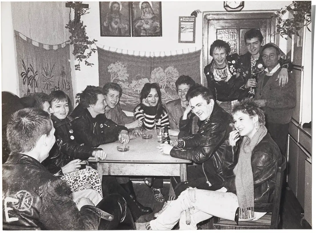 „Der Ronald Fleischmann hat einen Ausflug der Punks zu einem Schnapsbauern organisiert, da ist die komplette Pöbel-Band drauf. Außerdem die Gitarristin von der Frauenpunkband A-GEN 53 in der Mitte, daneben der Dirt Shit-Michi; rechts der Sven, Sänger von Pöbel; vorne links Tschuri, der Schlagzeuger, außerdem der Mofa und Joschi neben dem Schnapsbauern.“  