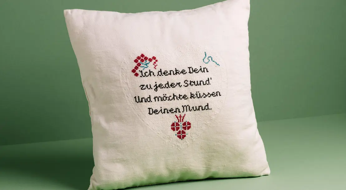 Per Postkarte hat eine Wienerin 1915 diese Botschaft an ihre Geliebte geschickt. Das Zitat wurde nun von der Künstlerin Anja Melzer auf einen Kaprizpolster gestickt, der in der neuen Ausstellung von QWIEN zu sehen ist. Foto: Gregor Hofbauer, QWIEN